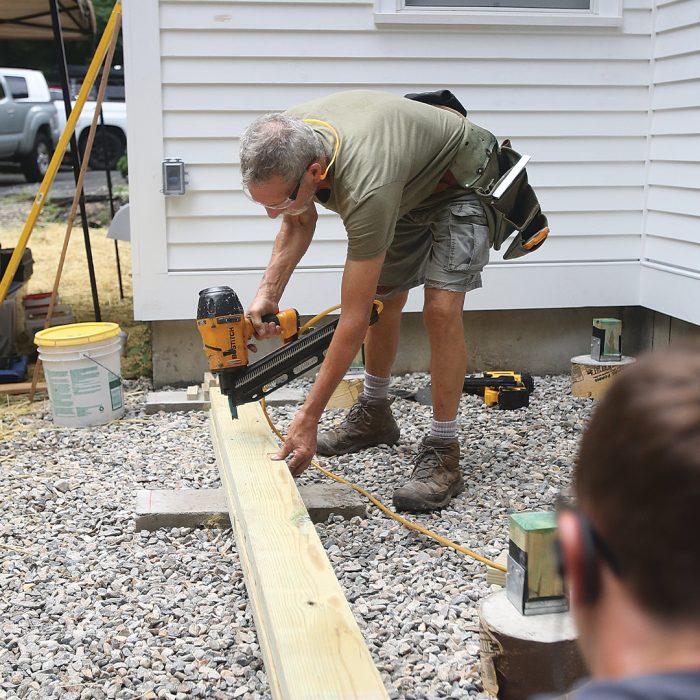 Man applying nails to a wooden beam with a nail gun.