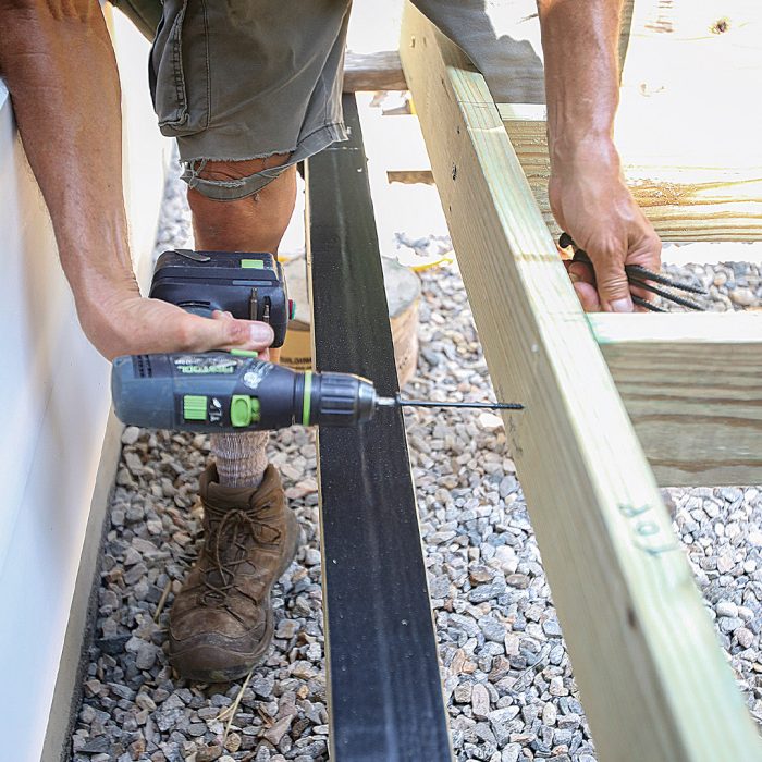 Hand driving a 5-in. structural screw into the deck frame.