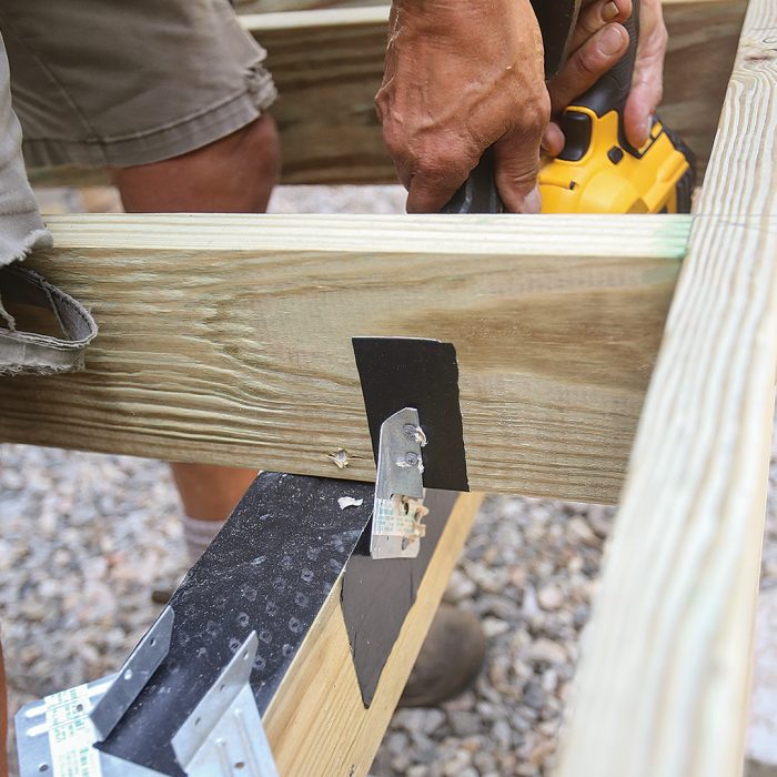 Man installing hurricane clips to the joist and beam for attachment and uplift protection.