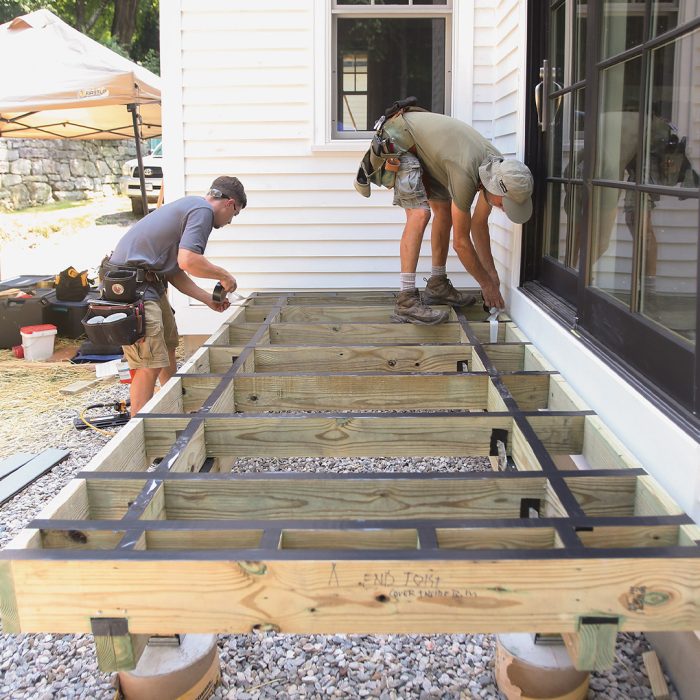 Two men measuring the length of the freestanding deck beam; one man is standing on the frame of the deck while the other is standing on the ground.