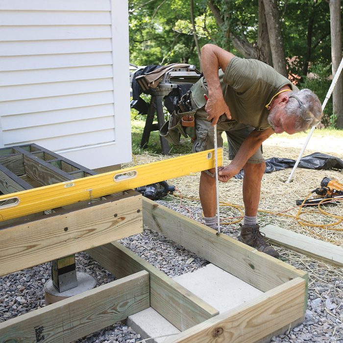 Man uses a level and measuring tape to make a notch in the deck's header boards.