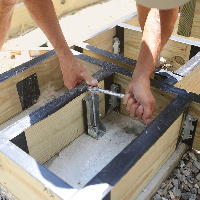 Man anchoring the bottom stair box to the footings with a screw and hand tool.