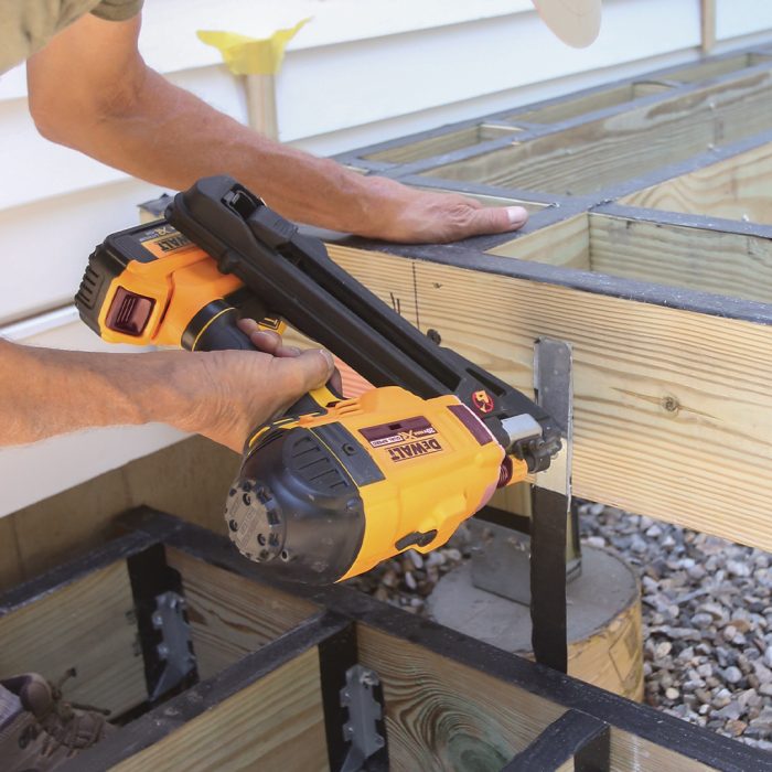 Man anchoring the bottom stair box to the footings with a nail gun.
