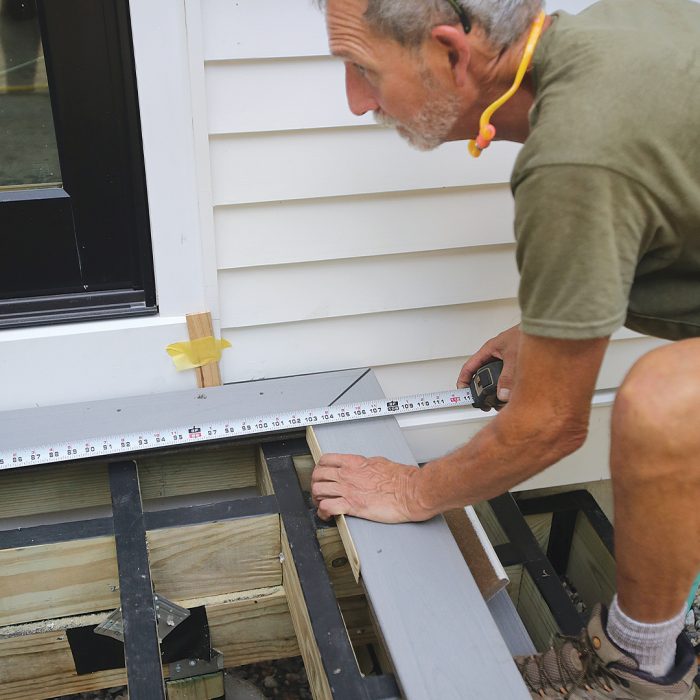 Man measures a deck using a measuring tape.