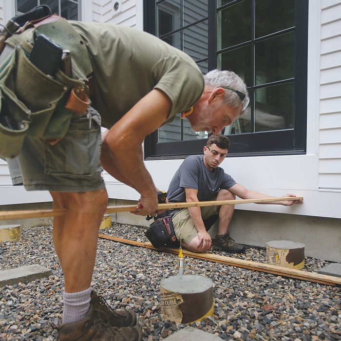 Man measuring with a plumb bob hung from a story pole to mark for post base anchors.