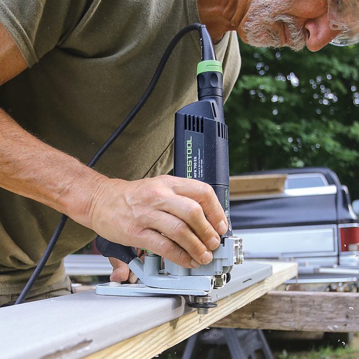 Man uses a router to cut a slot at each joist location.