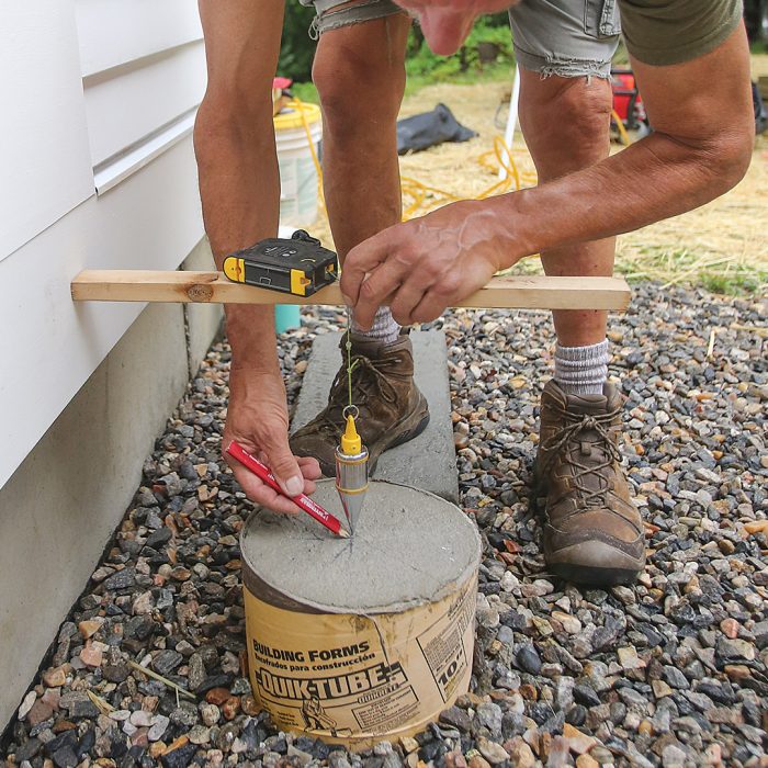 Man measuring with a plumb bob hung from a story pole to mark for post base anchors.