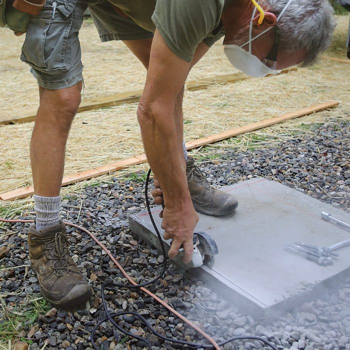 Man cutting a kerf with an angle grinder into a concrete deck footing.
