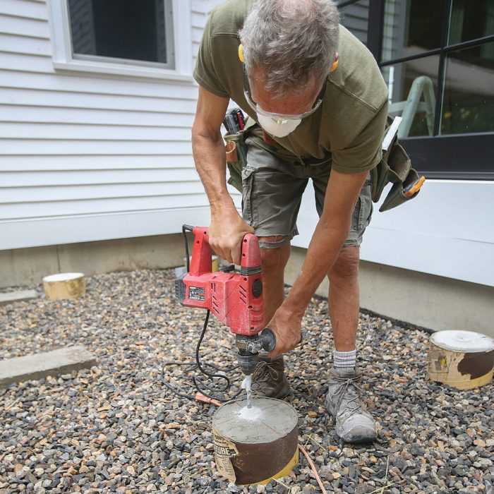 Man drilling holes for freestanding deck post-base anchors with a rotary hammer.