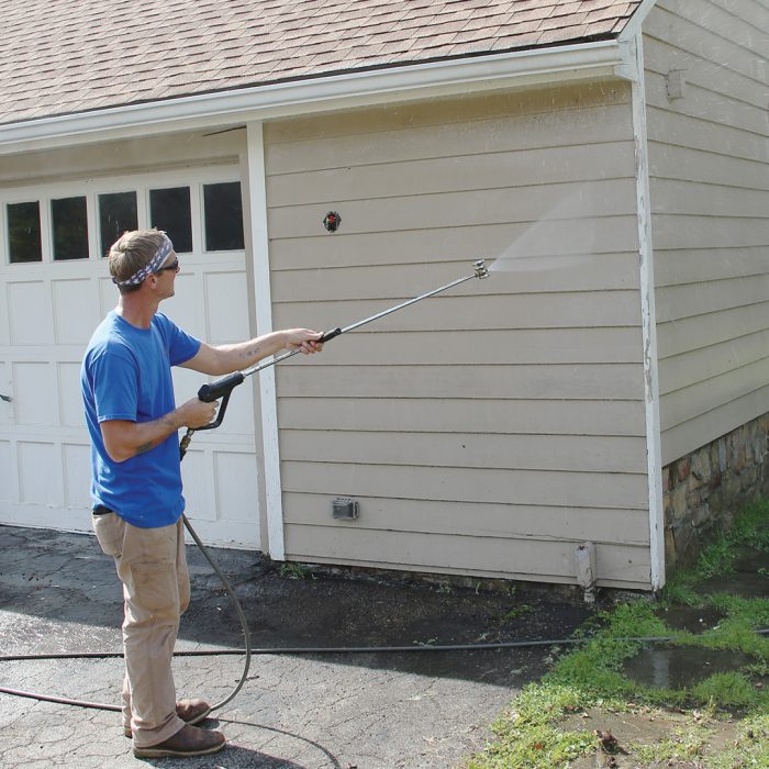 Man soft-washing the side of a house with beige siding.