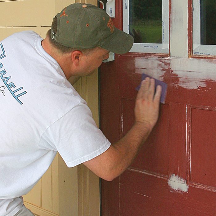 Man sanding surface of a door to ensure paint and primer stick to it properly.