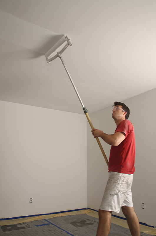 Man painting a ceiling with a paint roller.