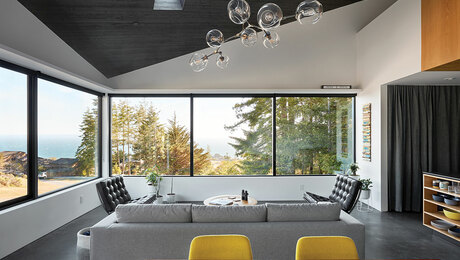 open concept living room with big windows, a gray couch, and a large light fixture