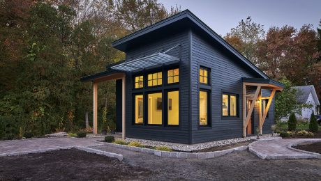 Prefab ADU with dark siding and glowing interior lights